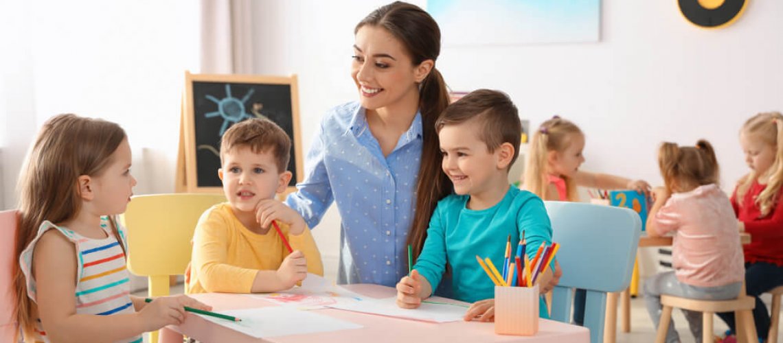 Little,Children,With,Kindergarten,Teacher,Drawing,At,Table,Indoors.,Learning